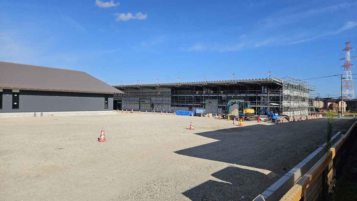 足場に囲まれた鉄骨の大きな建物と、手前のショベルカー